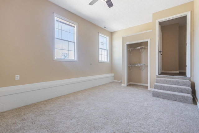 unfurnished bedroom featuring ceiling fan, a closet, light carpet, and a textured ceiling
