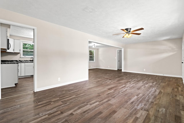 unfurnished living room with a textured ceiling, ceiling fan, sink, and dark wood-type flooring