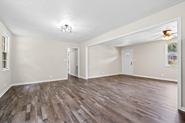 unfurnished living room with a textured ceiling, ceiling fan, and dark wood-type flooring