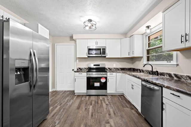 kitchen with sink, dark wood-type flooring, stainless steel appliances, a textured ceiling, and white cabinets