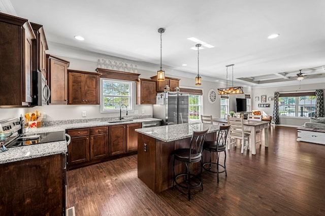 kitchen featuring pendant lighting, ceiling fan, appliances with stainless steel finishes, a kitchen island, and light stone counters