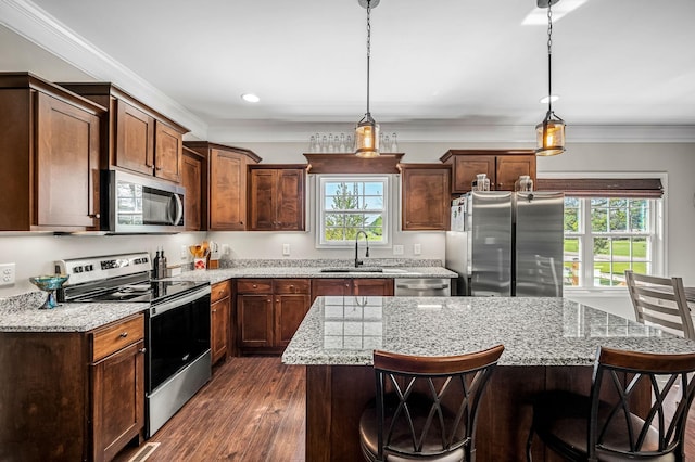 kitchen with pendant lighting, sink, a kitchen island, light stone counters, and stainless steel appliances