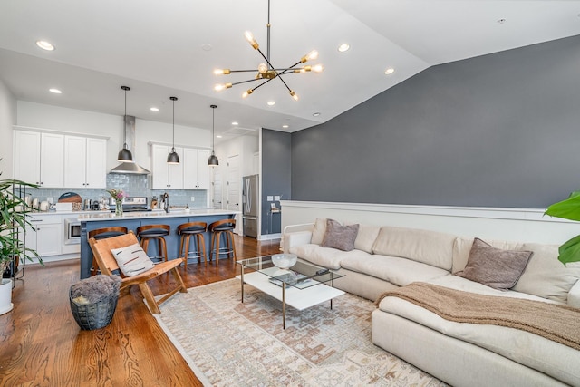 living room featuring a notable chandelier, light hardwood / wood-style flooring, and vaulted ceiling