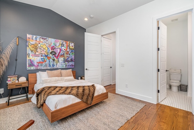 bedroom with a closet, ensuite bathroom, hardwood / wood-style floors, and vaulted ceiling