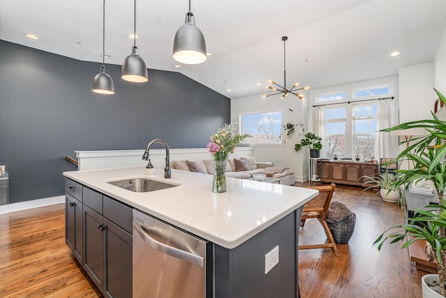 kitchen featuring light stone countertops, sink, stainless steel dishwasher, decorative light fixtures, and a kitchen island with sink