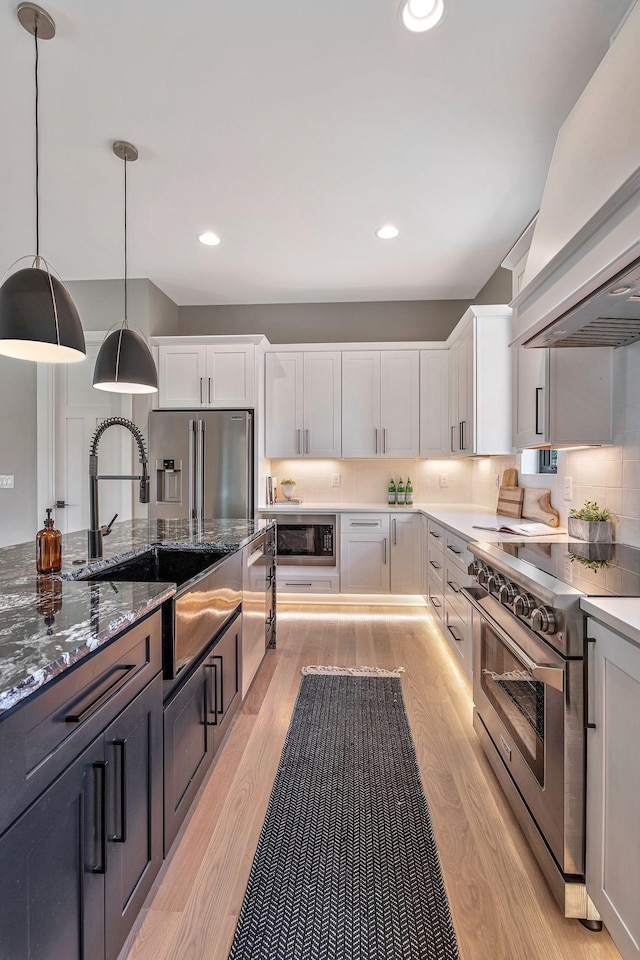 kitchen featuring premium range hood, premium appliances, sink, white cabinets, and hanging light fixtures