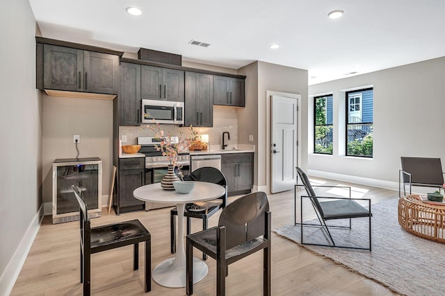 kitchen with wine cooler, backsplash, light hardwood / wood-style floors, dark brown cabinets, and appliances with stainless steel finishes