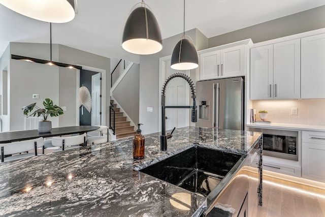 kitchen with sink, hanging light fixtures, high quality fridge, decorative backsplash, and white cabinets