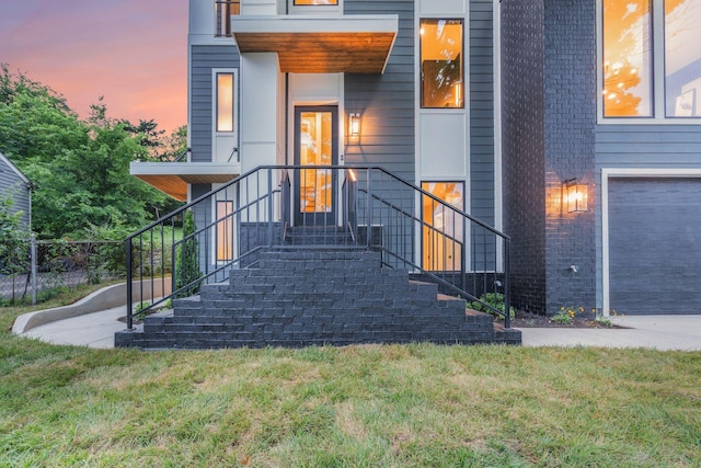 exterior entry at dusk with a lawn and a garage