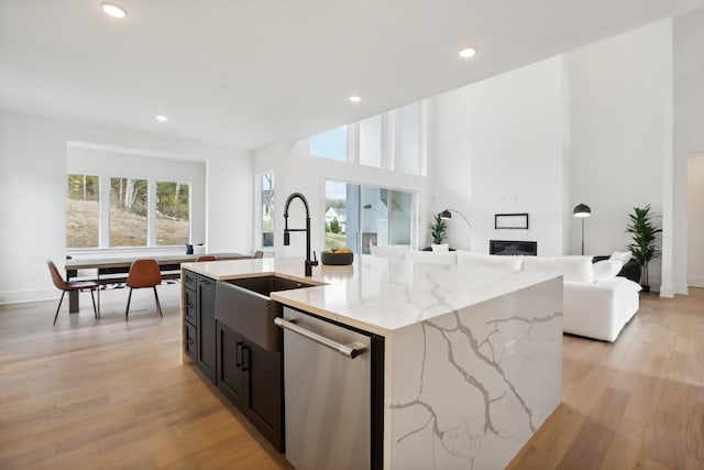 kitchen with dishwasher, sink, light stone counters, a fireplace, and a center island with sink