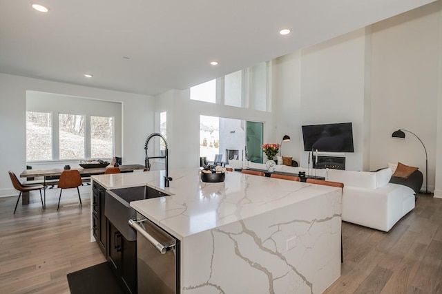 kitchen with dishwasher, sink, an island with sink, light hardwood / wood-style floors, and light stone counters