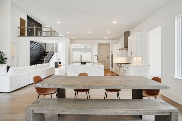 kitchen with sink, wall chimney exhaust hood, light hardwood / wood-style flooring, built in refrigerator, and white cabinets