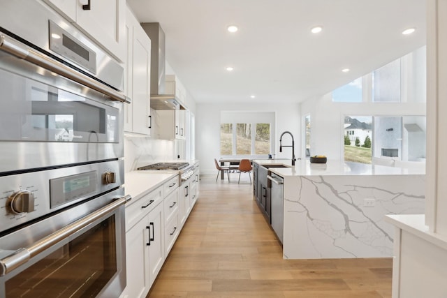 kitchen featuring wall chimney exhaust hood, light stone counters, white cabinetry, and backsplash