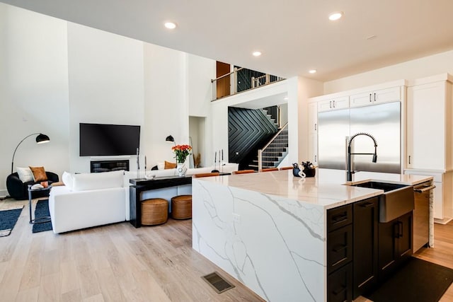 kitchen featuring white cabinets, light stone counters, light wood-type flooring, and built in fridge