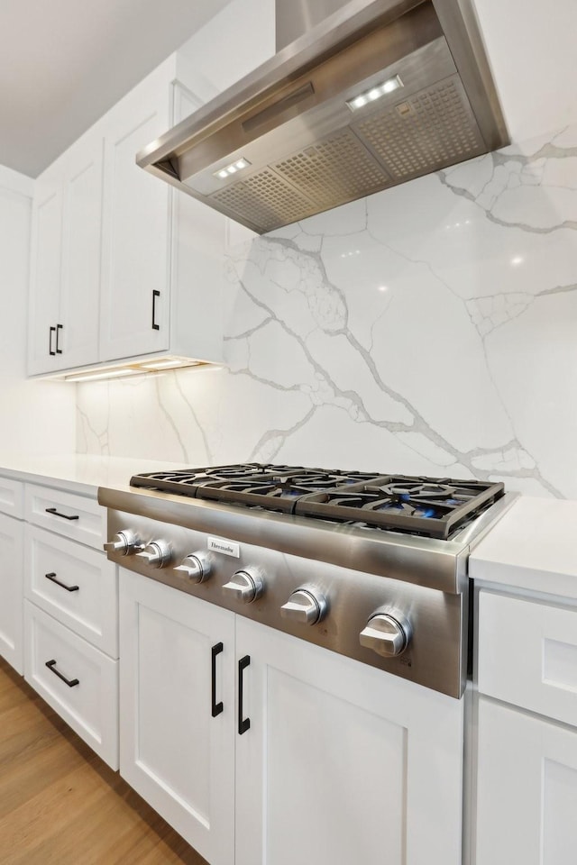 kitchen with decorative backsplash, light stone counters, stainless steel gas cooktop, and wall chimney range hood