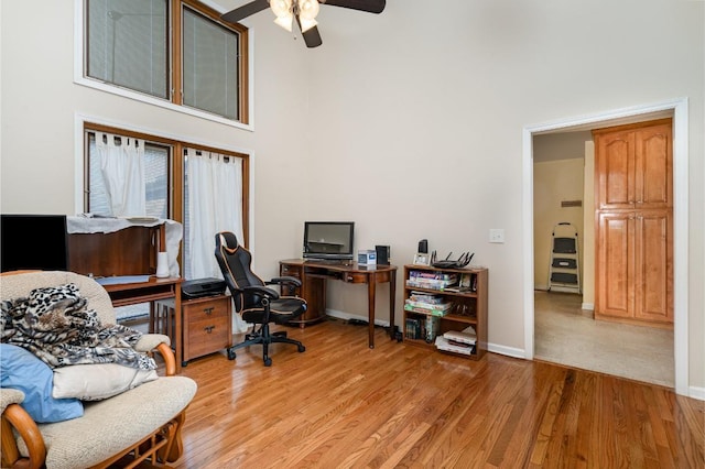 home office with ceiling fan, a towering ceiling, and light hardwood / wood-style flooring