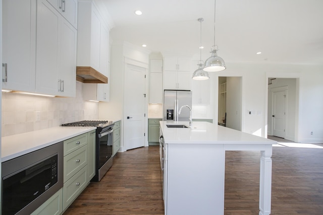 kitchen featuring sink, tasteful backsplash, hanging light fixtures, appliances with stainless steel finishes, and a kitchen island with sink