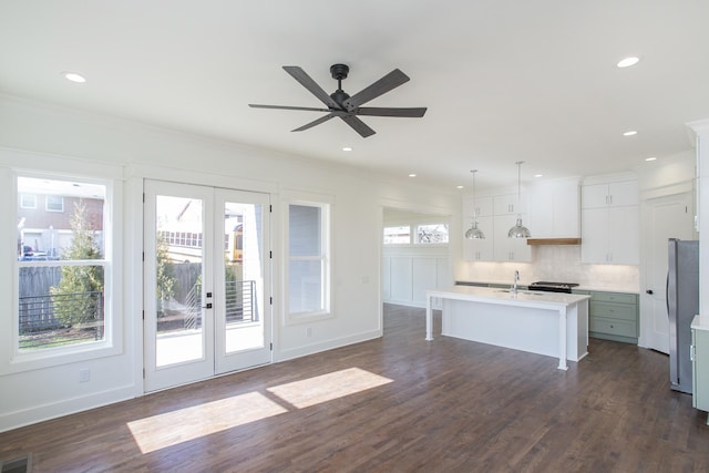 kitchen with decorative light fixtures, white cabinets, stainless steel fridge, a center island with sink, and french doors