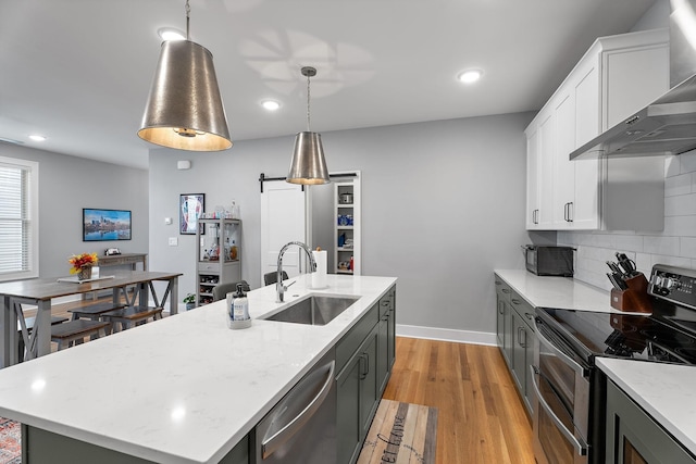 kitchen with sink, wall chimney exhaust hood, pendant lighting, a kitchen island with sink, and appliances with stainless steel finishes