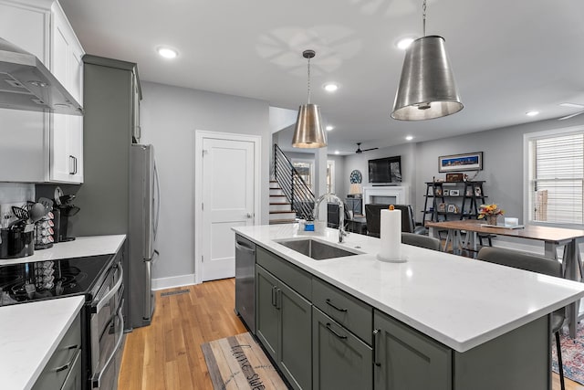 kitchen with pendant lighting, wall chimney range hood, sink, and an island with sink