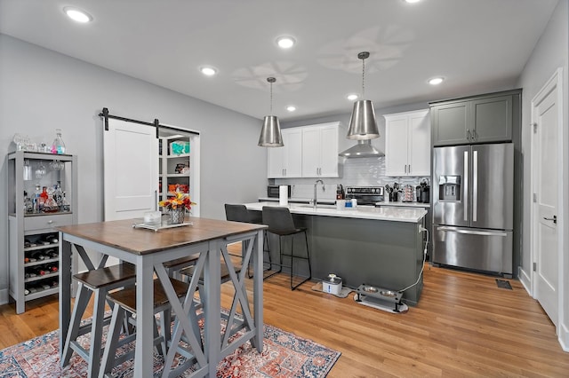 kitchen with appliances with stainless steel finishes, sink, a barn door, decorative light fixtures, and light hardwood / wood-style flooring