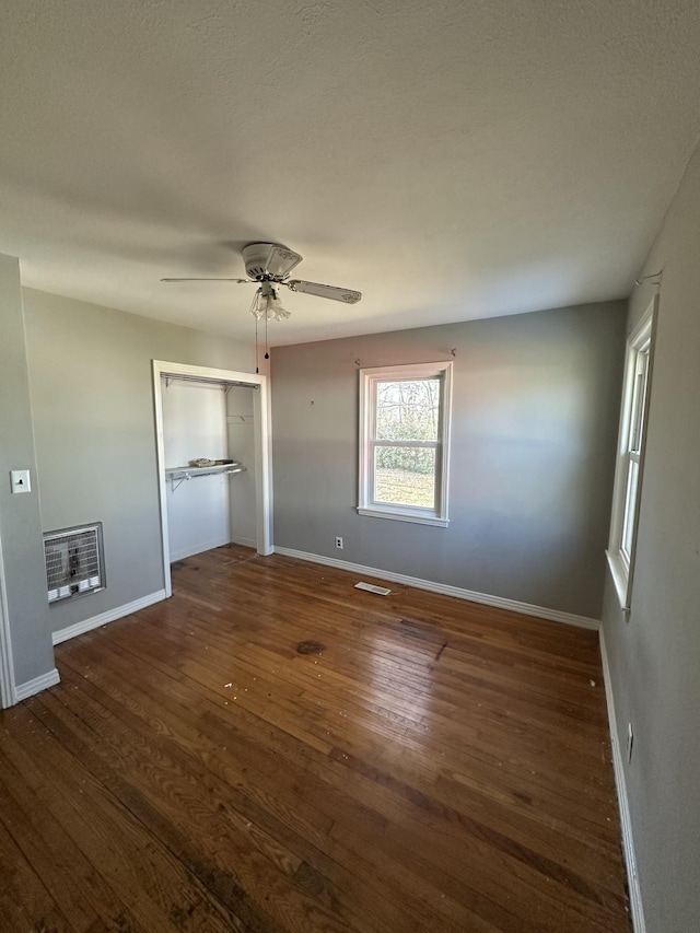 unfurnished bedroom with dark hardwood / wood-style flooring, ceiling fan, a closet, and heating unit