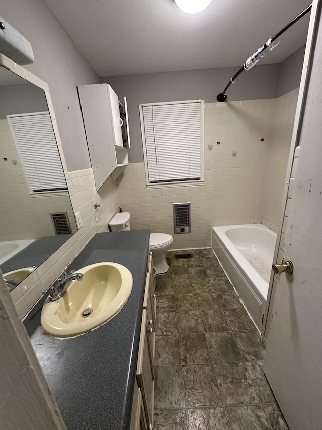 full bathroom with toilet, tile walls, heating unit, tiled shower / bath combo, and vanity