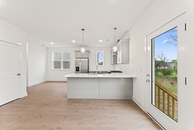 kitchen featuring decorative light fixtures, backsplash, kitchen peninsula, stainless steel refrigerator with ice dispenser, and light wood-type flooring