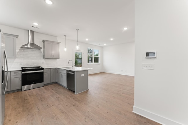 kitchen featuring decorative light fixtures, gray cabinets, kitchen peninsula, stainless steel appliances, and wall chimney exhaust hood