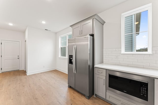 kitchen with backsplash, stainless steel refrigerator with ice dispenser, built in microwave, and gray cabinetry