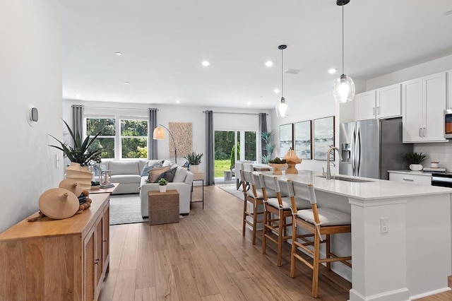 kitchen with a kitchen island with sink, sink, stainless steel fridge, decorative light fixtures, and white cabinetry