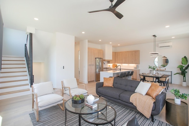 living room featuring light wood-type flooring, a wall unit AC, ceiling fan, and sink