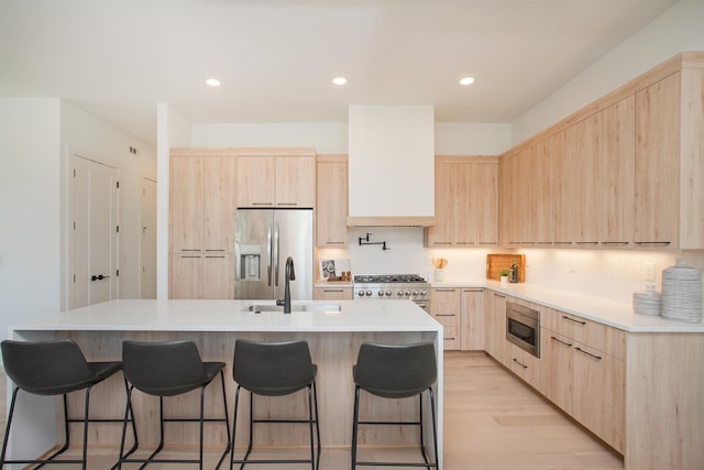 kitchen with sink, stainless steel appliances, a kitchen island with sink, light brown cabinetry, and custom exhaust hood