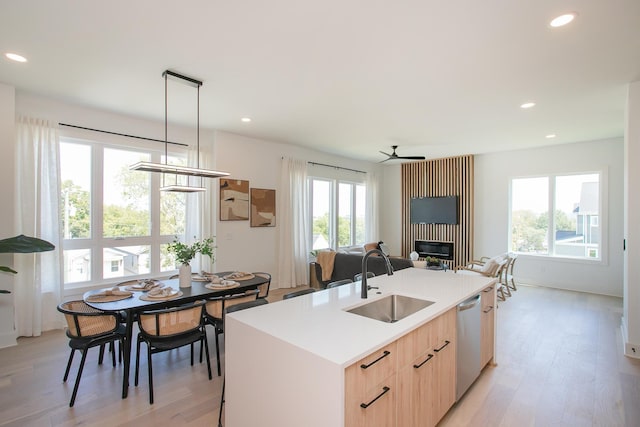 kitchen featuring sink, hanging light fixtures, stainless steel dishwasher, light brown cabinetry, and a center island with sink