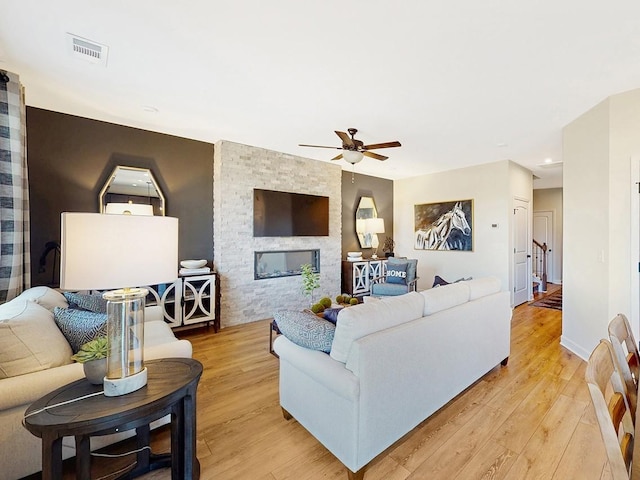 living room featuring light wood-type flooring, a stone fireplace, and ceiling fan