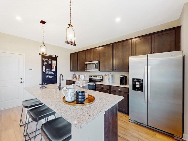 kitchen with a center island with sink, pendant lighting, dark brown cabinetry, and stainless steel appliances