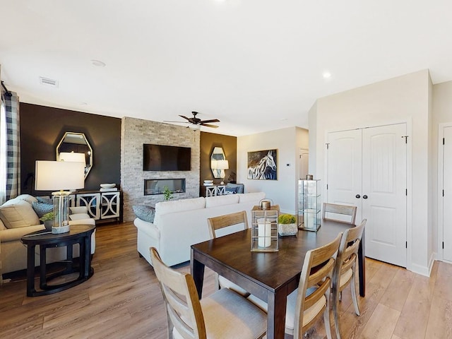 dining area with a stone fireplace, ceiling fan, and light wood-type flooring