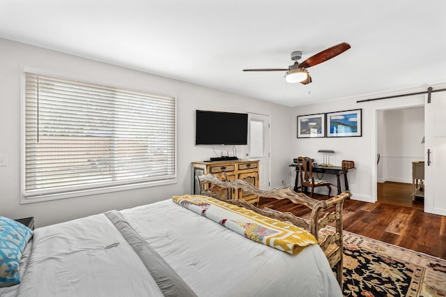 bedroom with ceiling fan, a barn door, and dark wood-type flooring