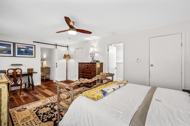 bedroom featuring dark hardwood / wood-style flooring, a barn door, ensuite bathroom, and ceiling fan