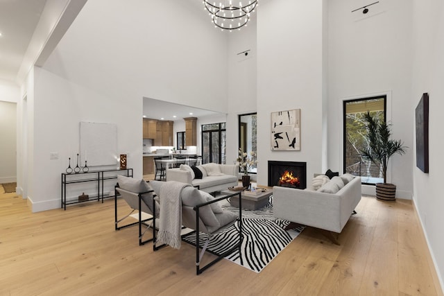 living room with an inviting chandelier, a towering ceiling, and light hardwood / wood-style floors