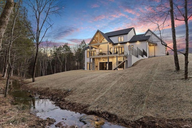 back house at dusk featuring a balcony and a lawn