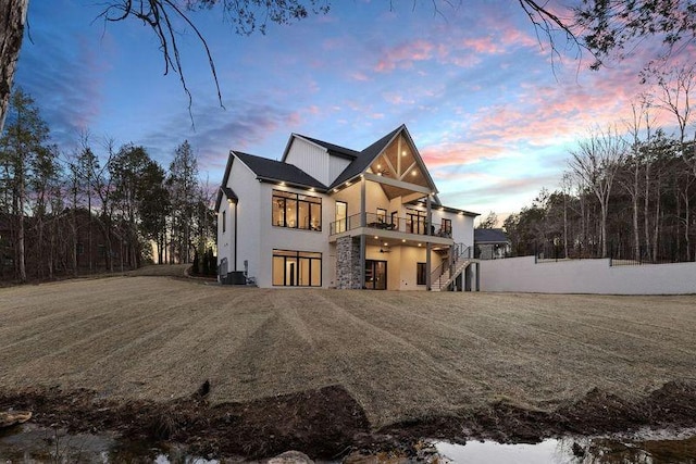 back house at dusk featuring a lawn and a balcony