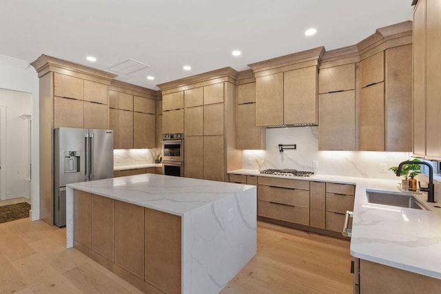 kitchen with sink, stainless steel appliances, a center island, light stone counters, and light hardwood / wood-style floors