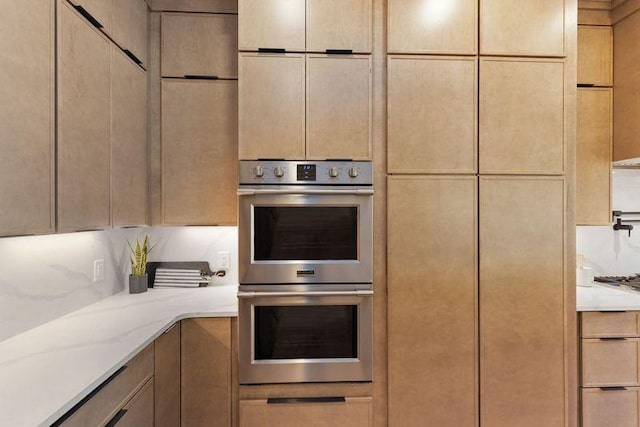 kitchen with double oven, decorative backsplash, light stone countertops, and light brown cabinets