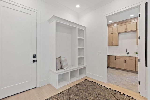 mudroom with sink, built in shelves, and light wood-type flooring