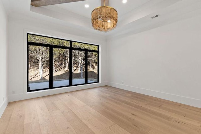 empty room with light hardwood / wood-style flooring, a raised ceiling, and a chandelier