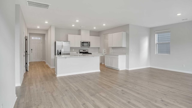 kitchen with light wood-type flooring, stainless steel appliances, white cabinetry, and an island with sink