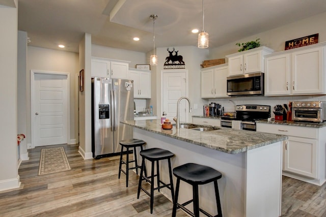 kitchen featuring pendant lighting, stone counters, white cabinets, an island with sink, and appliances with stainless steel finishes