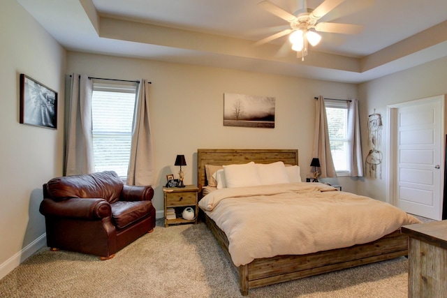 bedroom featuring a tray ceiling, multiple windows, ceiling fan, and light carpet