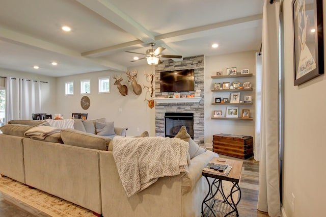 living room with hardwood / wood-style floors, ceiling fan, a stone fireplace, and beamed ceiling